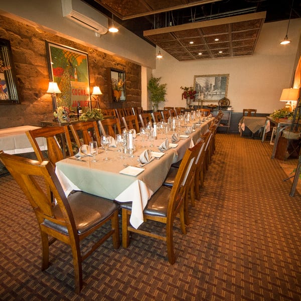 A long dining table set for a formal meal in a restaurant with stone walls and warm lighting.