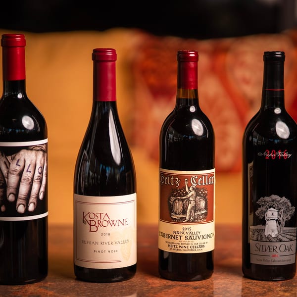 Four bottles of red wine, including Kosta Browne, Heitz Cellar, and Silver Oak, on a wooden surface.