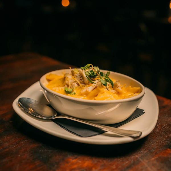 Creamy mac and cheese with crab meat and microgreens in a white bowl on a wooden table.