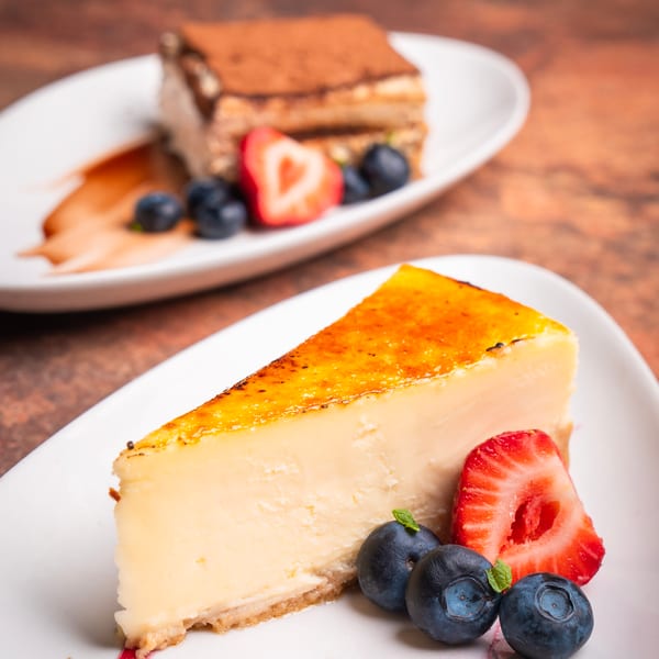 Two dessert plates: a slice of cheesecake with berries and a tiramisu with fruit.