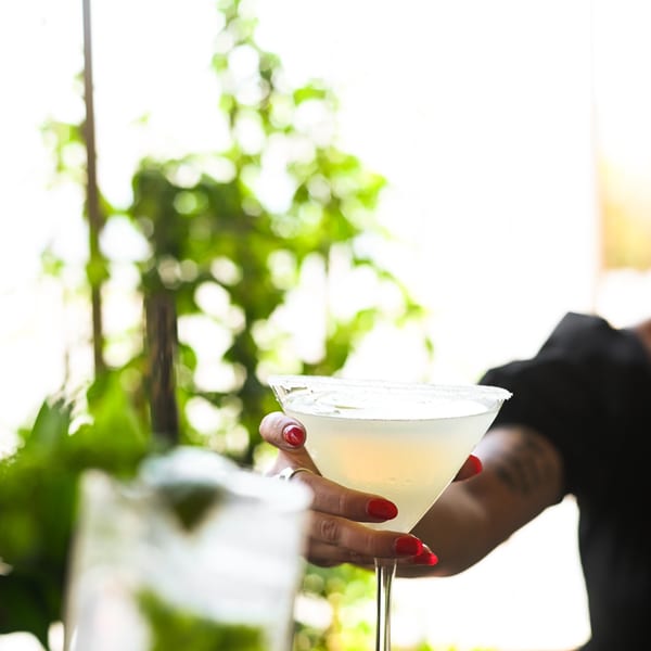 A person with red nails holds a margarita with a salted rim, another drink blurred in the foreground.