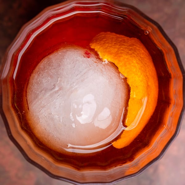 Overhead view of a cocktail with a large ice sphere and an orange peel garnish.
