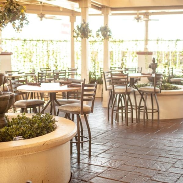 An outdoor patio dining area with tables, chairs, and a decorative fountain surrounded by greenery.