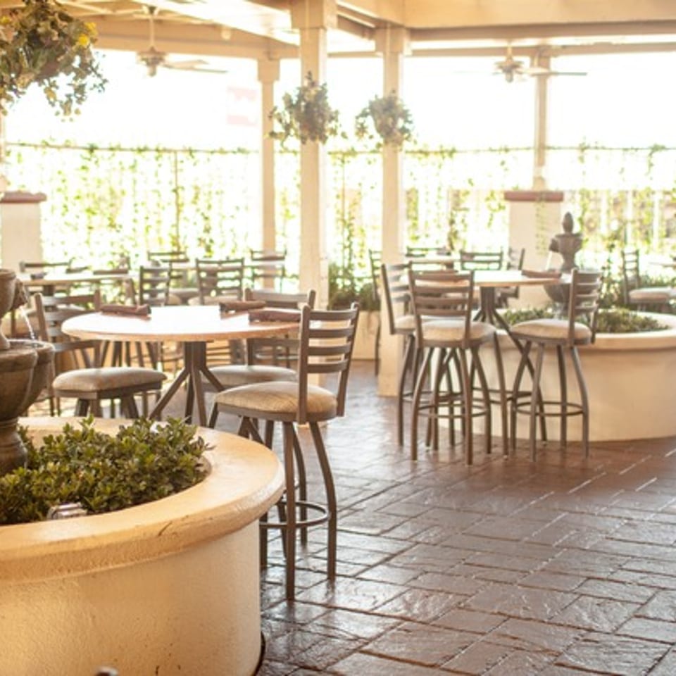 An outdoor patio dining area with tables, chairs, and a decorative fountain surrounded by greenery.