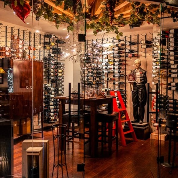 A glass-enclosed wine cellar with numerous bottles, a table, and a butler statue.