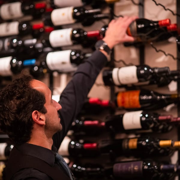 Sommelier reaching for a bottle of red wine from a large, well-stocked wine rack.