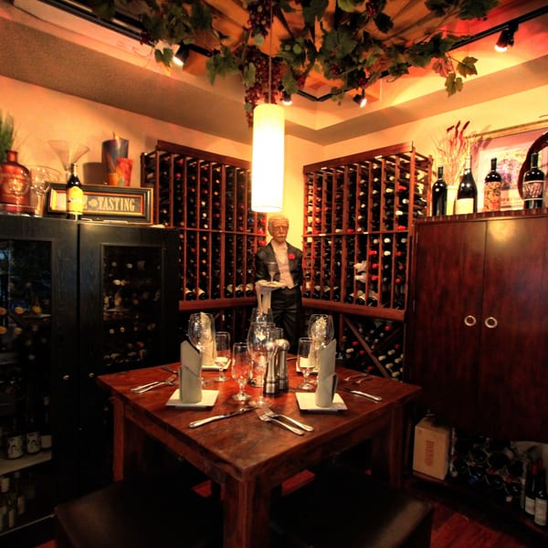 A cozy private dining room with a set table, surrounded by wine racks and a waiter statue.