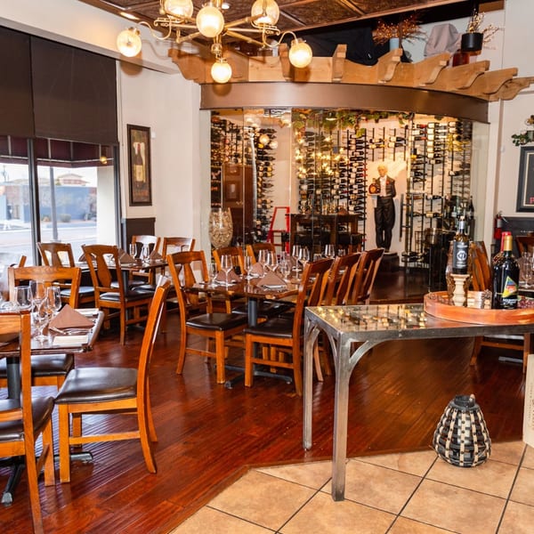 Elegant restaurant dining room with set tables, large windows, and a prominent wine display.