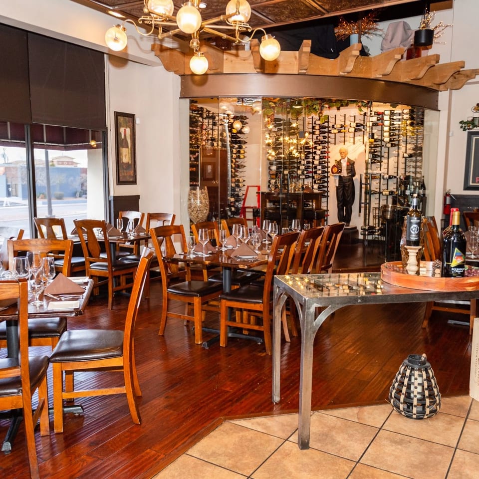 Elegant restaurant dining room with set tables, a large wine display, and a window view.